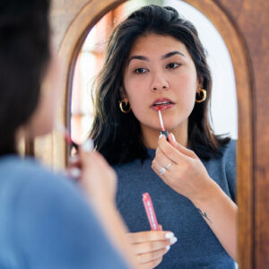 Woman applying lip gloss in mirror.