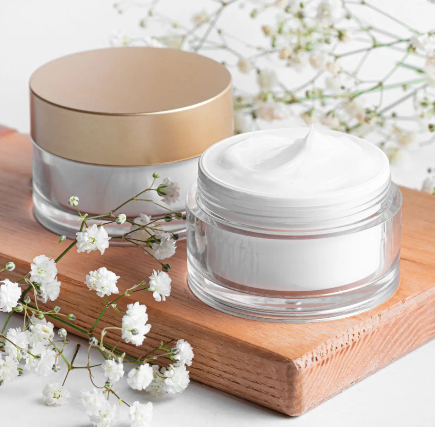 Cream jars with flowers on wooden board.